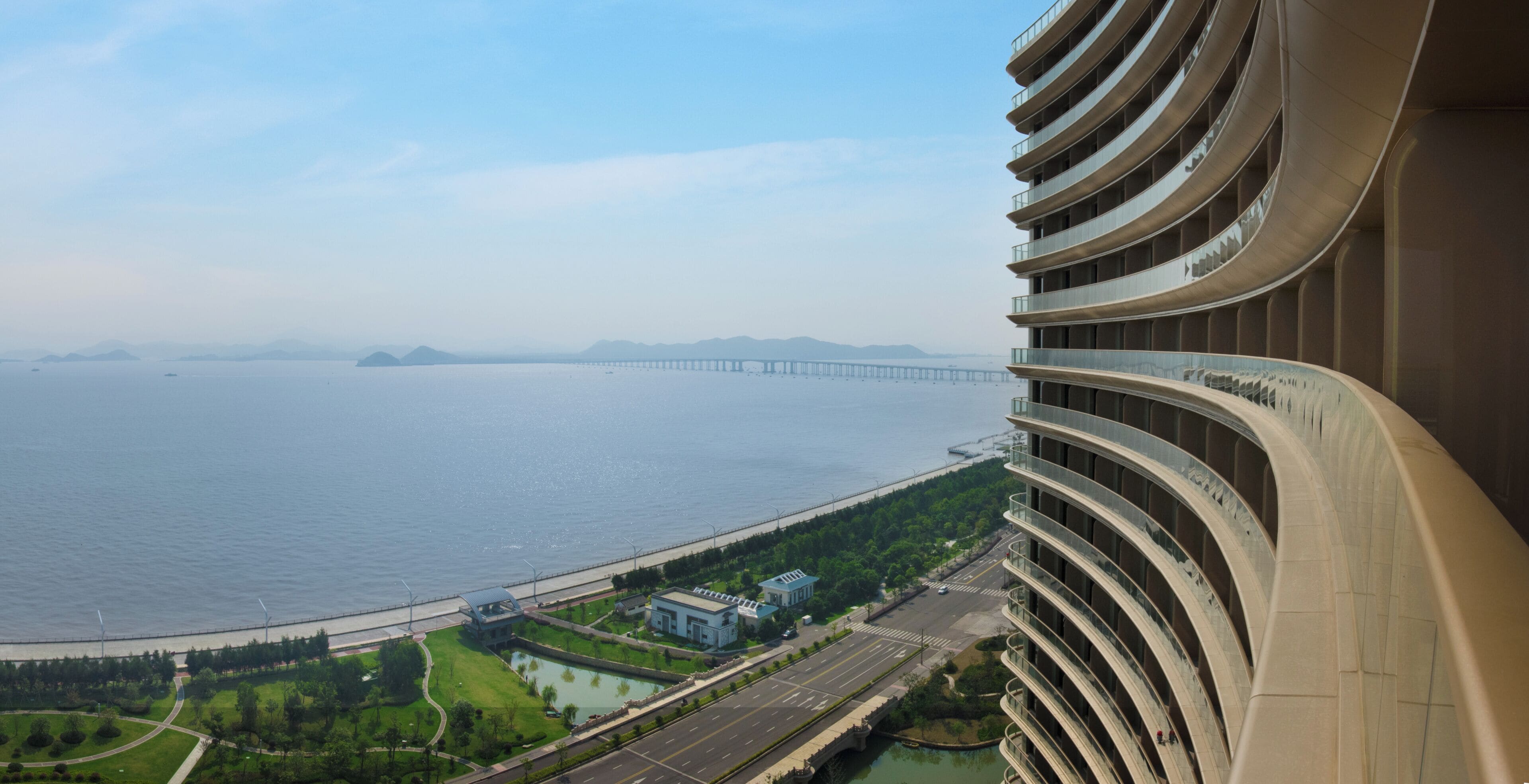 A high-rise building with a curved facade overlooking a river and a bridge.