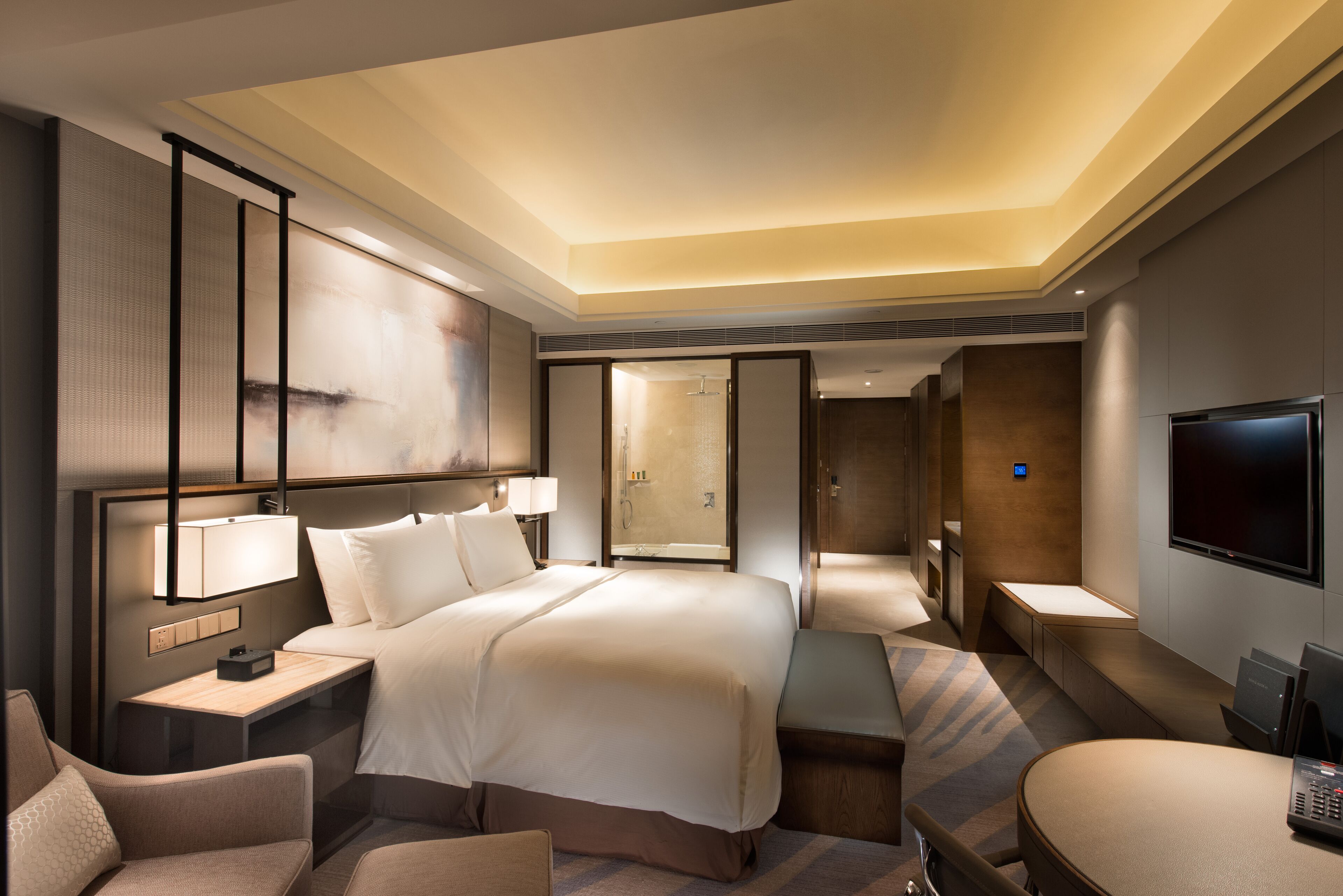 A modern hotel room with a large bed, bedside tables, a desk, a seating area, and a TV.