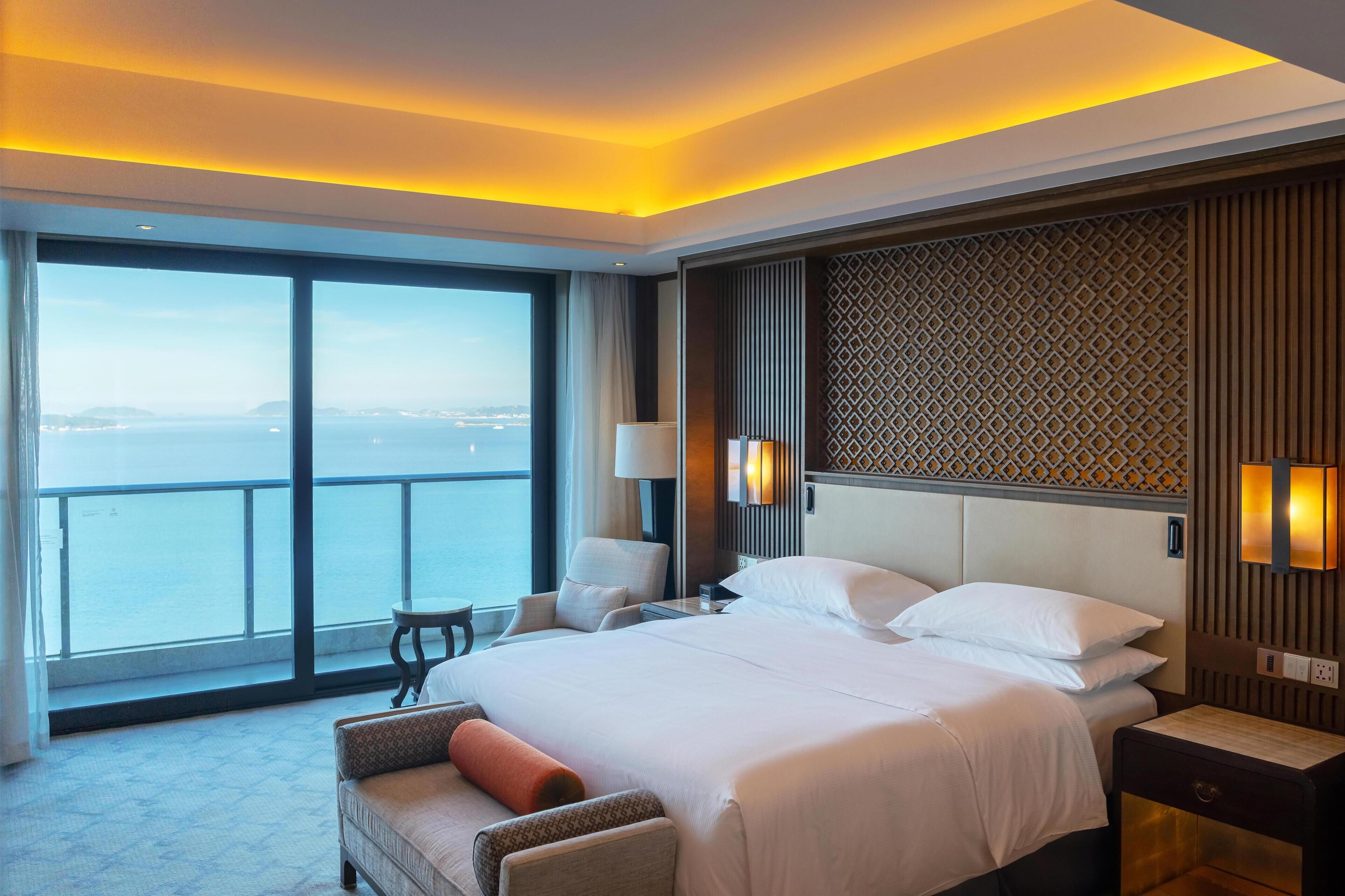 A hotel room with a large bed, a view of the sea, and a balcony.