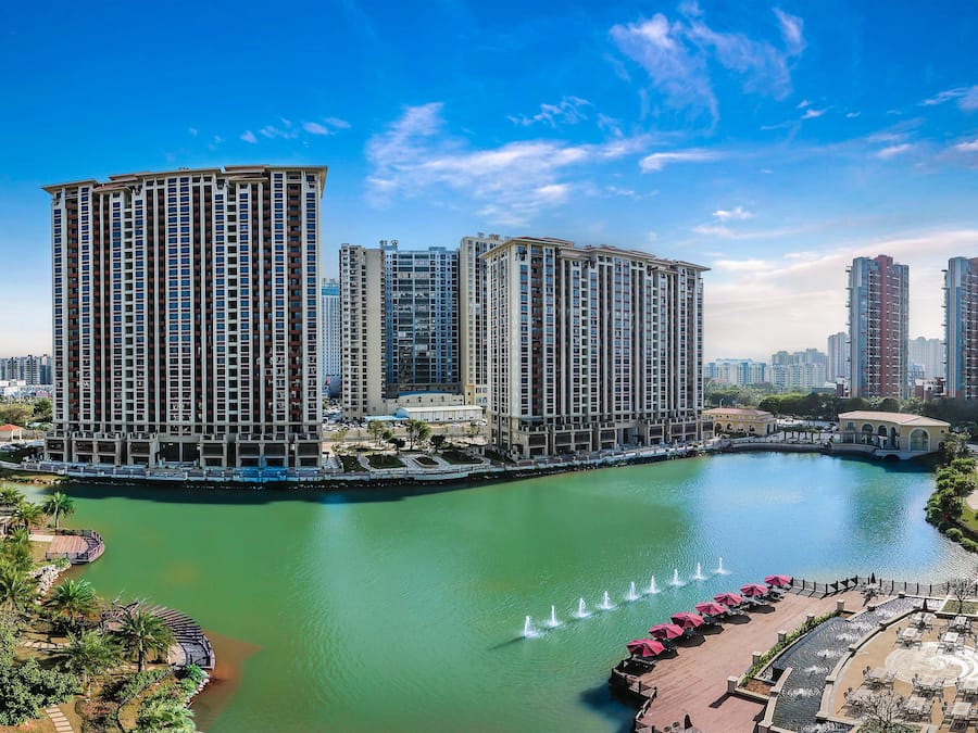 A high-rise hotel with multiple floors, a central courtyard with fountains, and a surrounding body of water.
