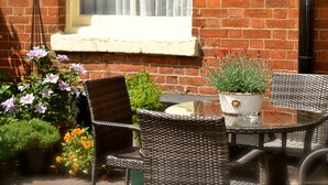 A patio with wicker chairs and a glass table, surrounded by potted plants and flowers. - The Queen Hotel (Olney)