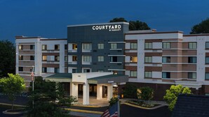 A multi-story hotel with a flat roof, a sign reading 'COURTYARD BY MARRIOTT,' and a parking lot with an American flag.
