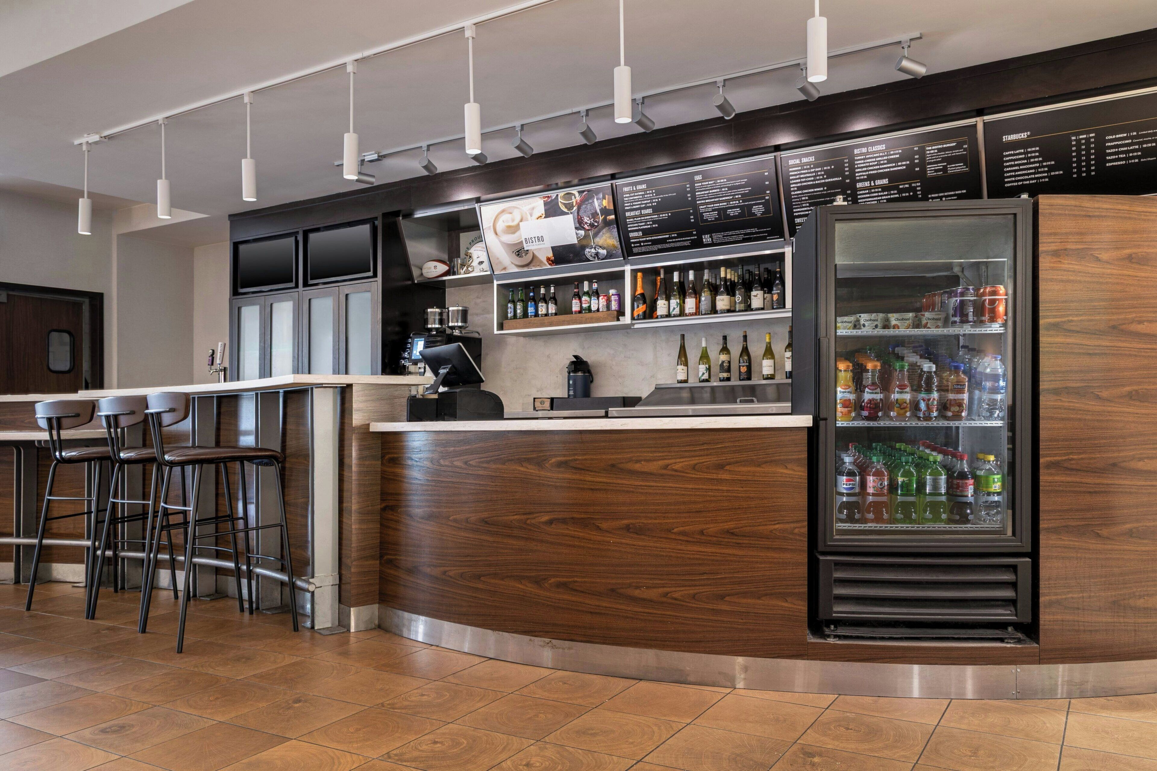 Zona de bar con taburetes, un refrigerador lleno de bebidas y una pizarra con la carta.