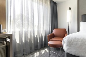 Une chambre d’hôtel comprenant un lit, une chaise, un bureau avec une machine à café et une lampe.