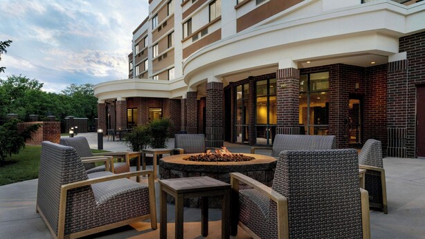 A hotel patio with outdoor seating, a fire pit, and a brick facade.