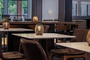 Un espace de restauration moderne, doté de tables et de chaises, de lampes décoratives et de grandes fenêtres offrant une vue sur la verdure.