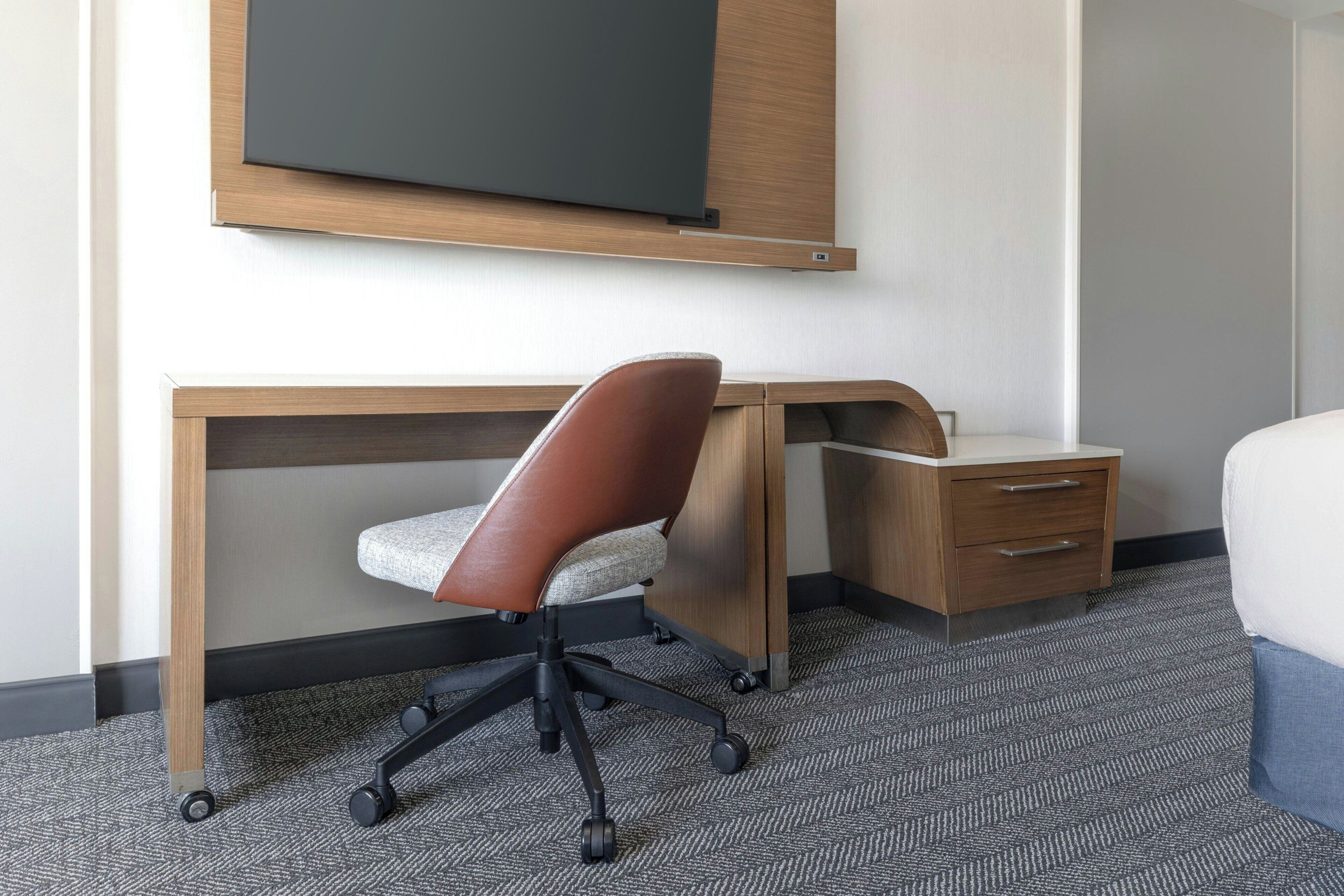 A hotel room with a desk, chair, and a bed.