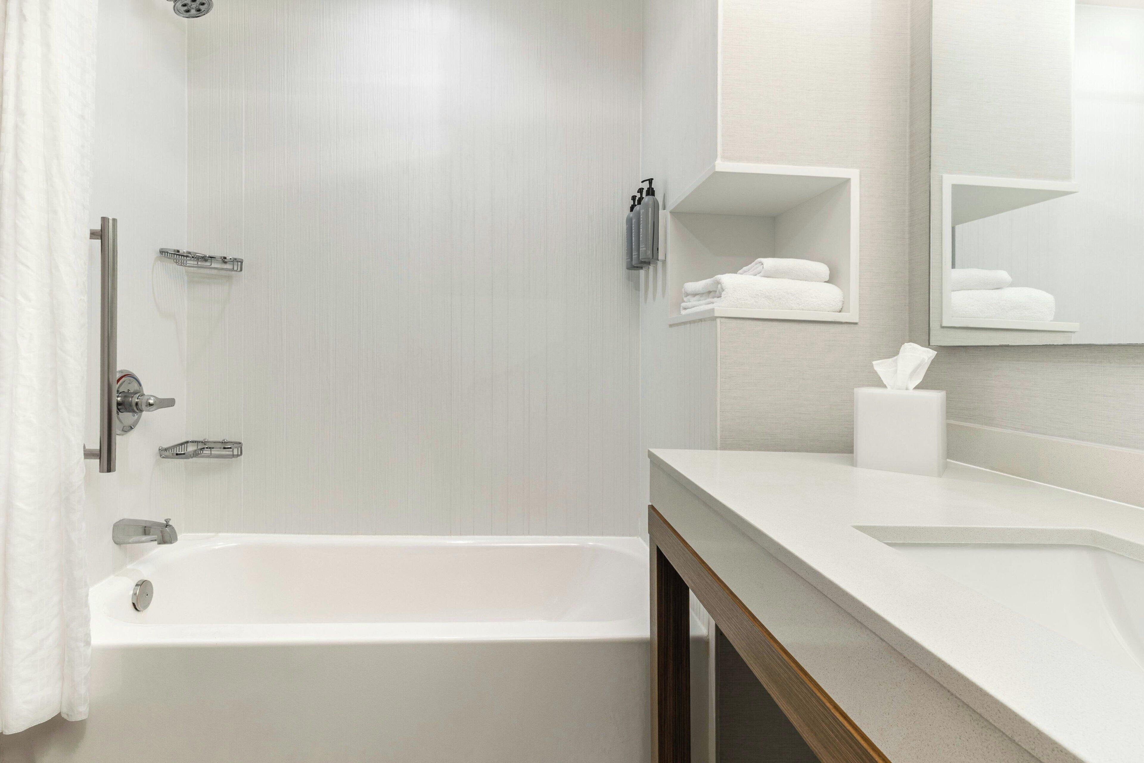 A modern bathroom with a bathtub, a shower, a vanity with a mirror, and a towel rack.
