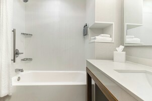 A modern bathroom with a bathtub, a shower, a vanity with a mirror, and a towel rack.