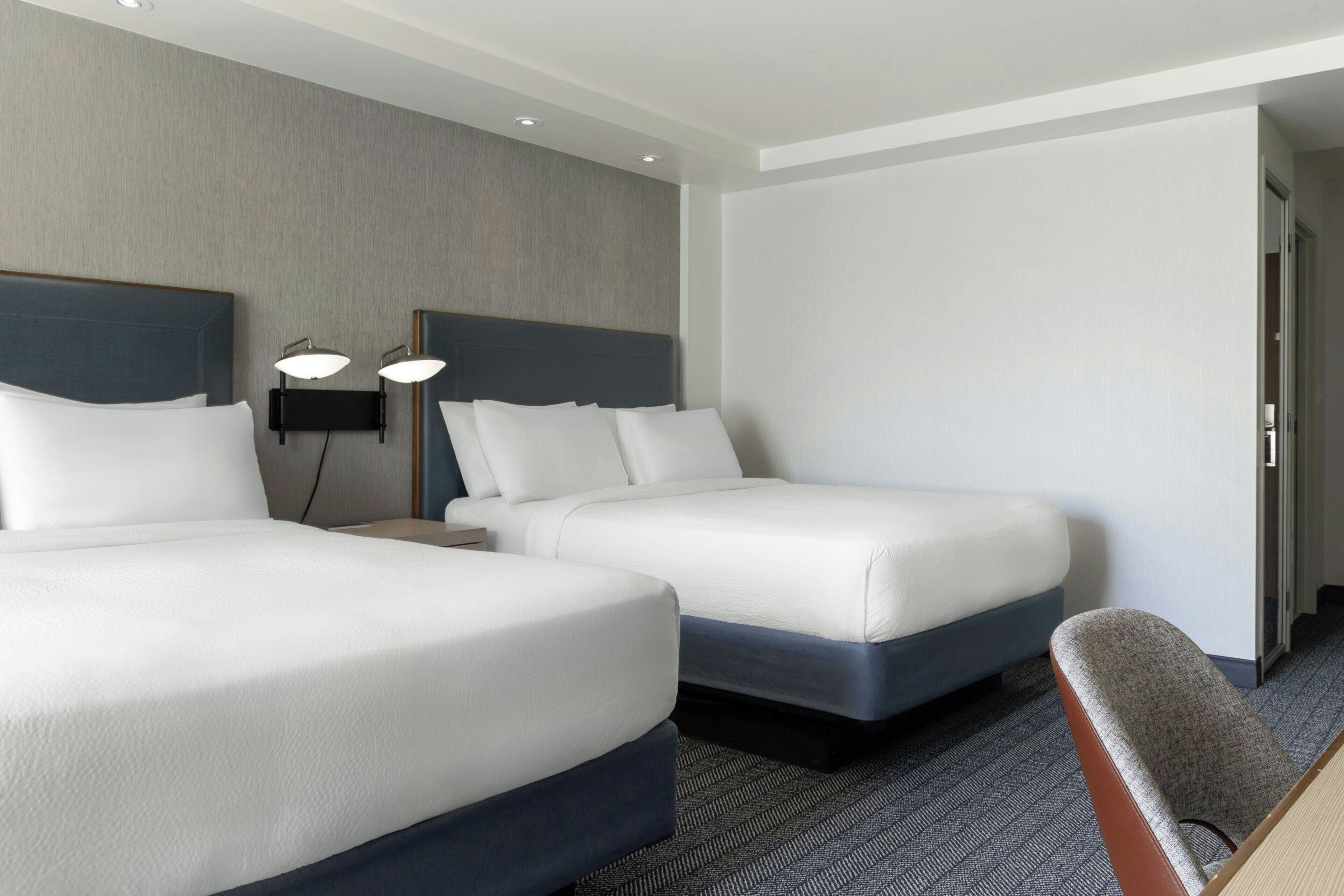 Habitación de hotel con dos camas, una mesita de noche, una silla y una puerta.