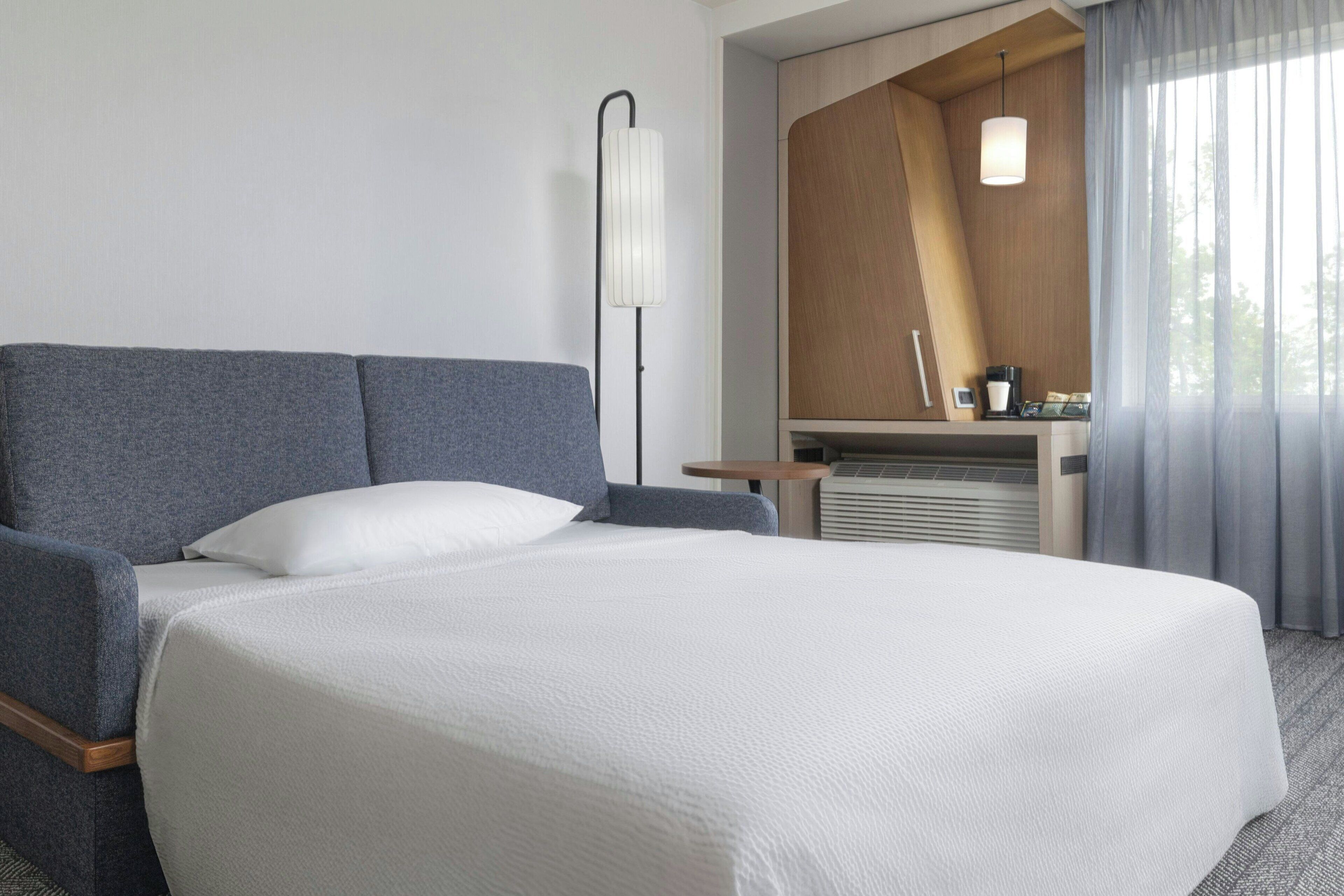 A hotel room with a large bed, a sofa, a desk, and a window with curtains.