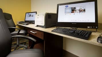 Un espacio de trabajo en un hotel con dos computadoras de escritorio, un teclado y un ratón sobre una mesa, y sillas alrededor.