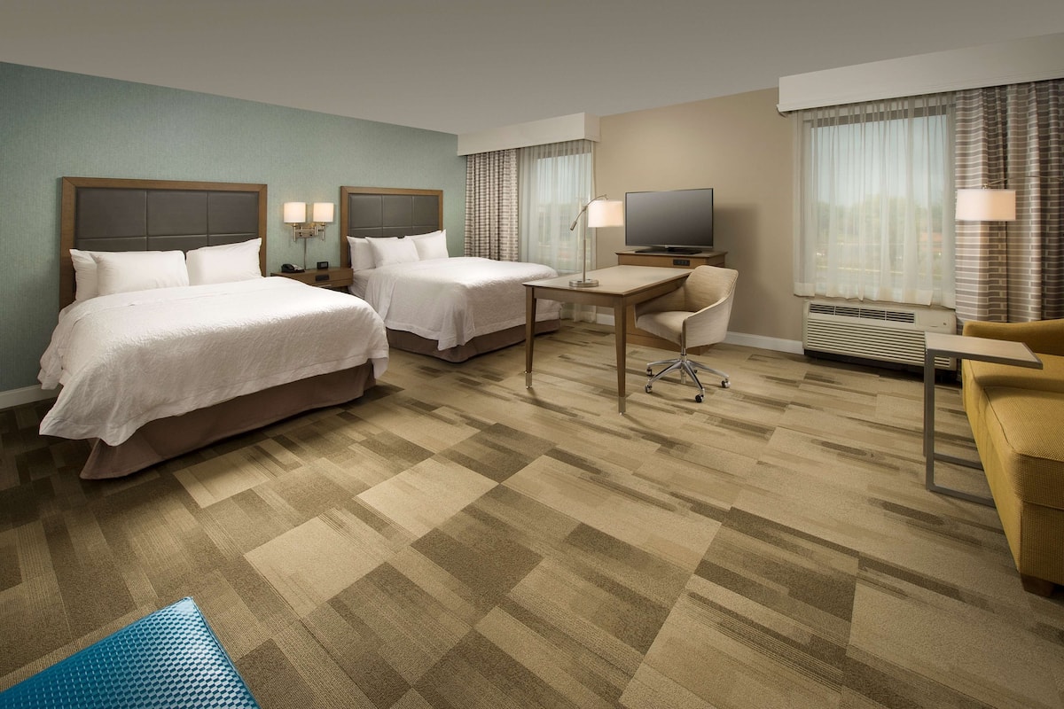 A hotel room with two beds, a desk, a TV, and a chair.