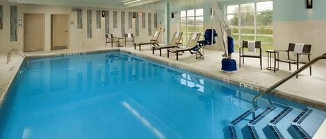 A swimming pool with clear blue water, surrounded by lounge chairs and a sunshade.