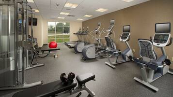 A gym with treadmills, elliptical machines, a weight bench, and free weights.