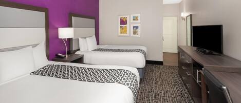 Une chambre d’hôtel avec deux lits, une télévision, une commode et des œuvres d’art accrochées au mur.
