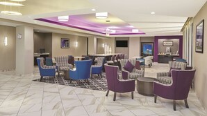 A spacious lobby with a marble floor, purple and blue upholstered chairs, a reception desk, and a large dining area with a view of a building. - La Quinta Inn & Suites by Wyndham Springfield IL (Springfield)