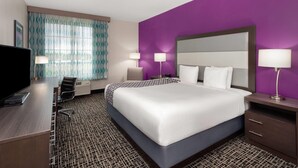 A hotel room with a large bed, a desk with a computer, two bedside lamps, and a window with patterned curtains.