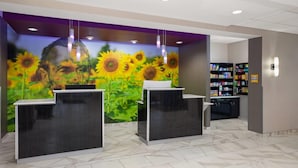 A reception area with a large mural of sunflowers, a reception desk, and a vending machine. - La Quinta Inn & Suites by Wyndham Springfield IL (Springfield)