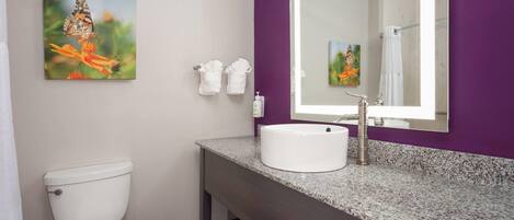 A bathroom with a white toilet, a granite countertop, a white sink, a large mirror, and two wall-mounted towels.