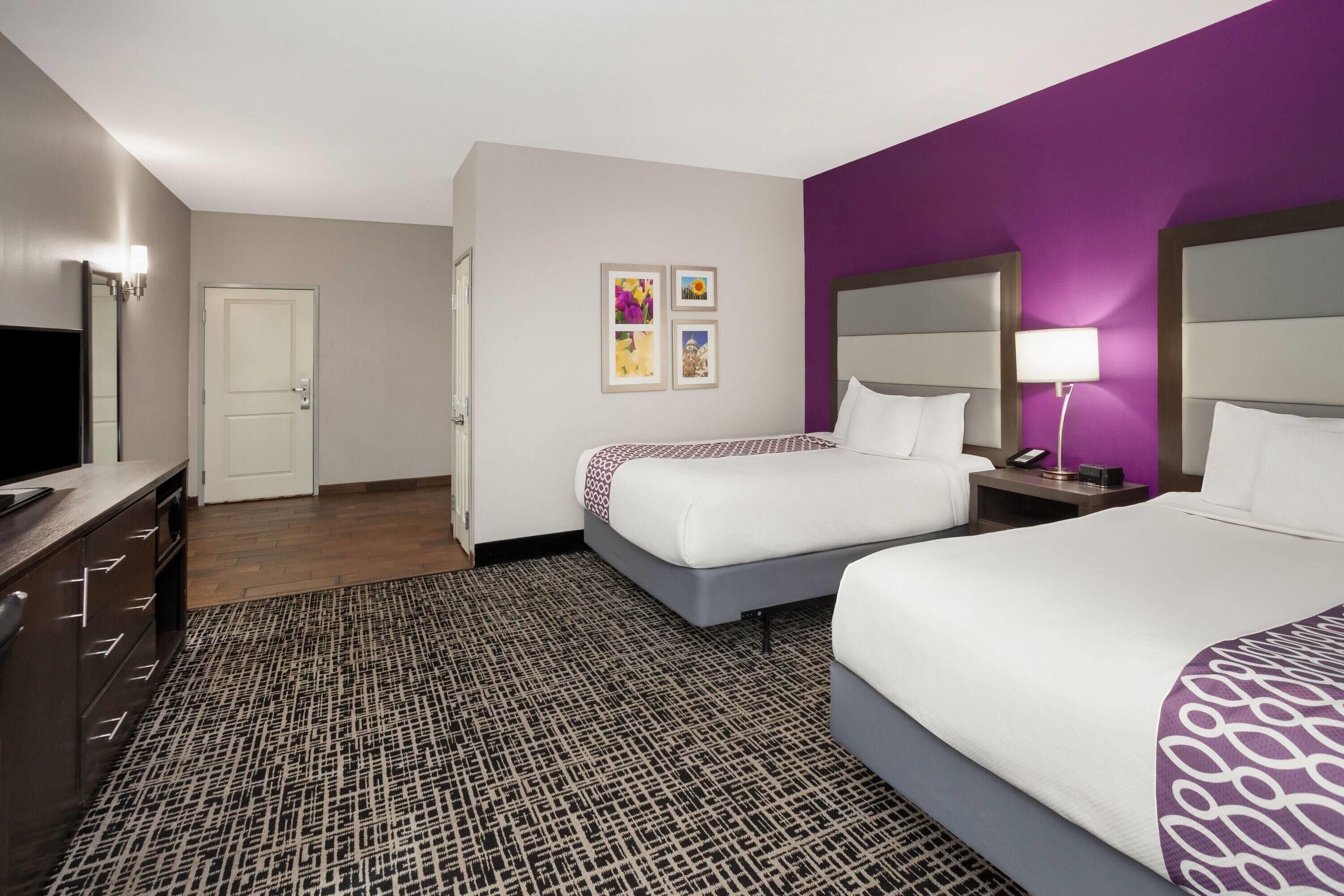 A hotel room with two beds, a desk, a TV, and a patterned rug.
