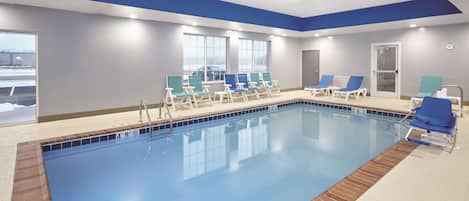 A swimming pool with lounge chairs, a tiled deck, and large windows.