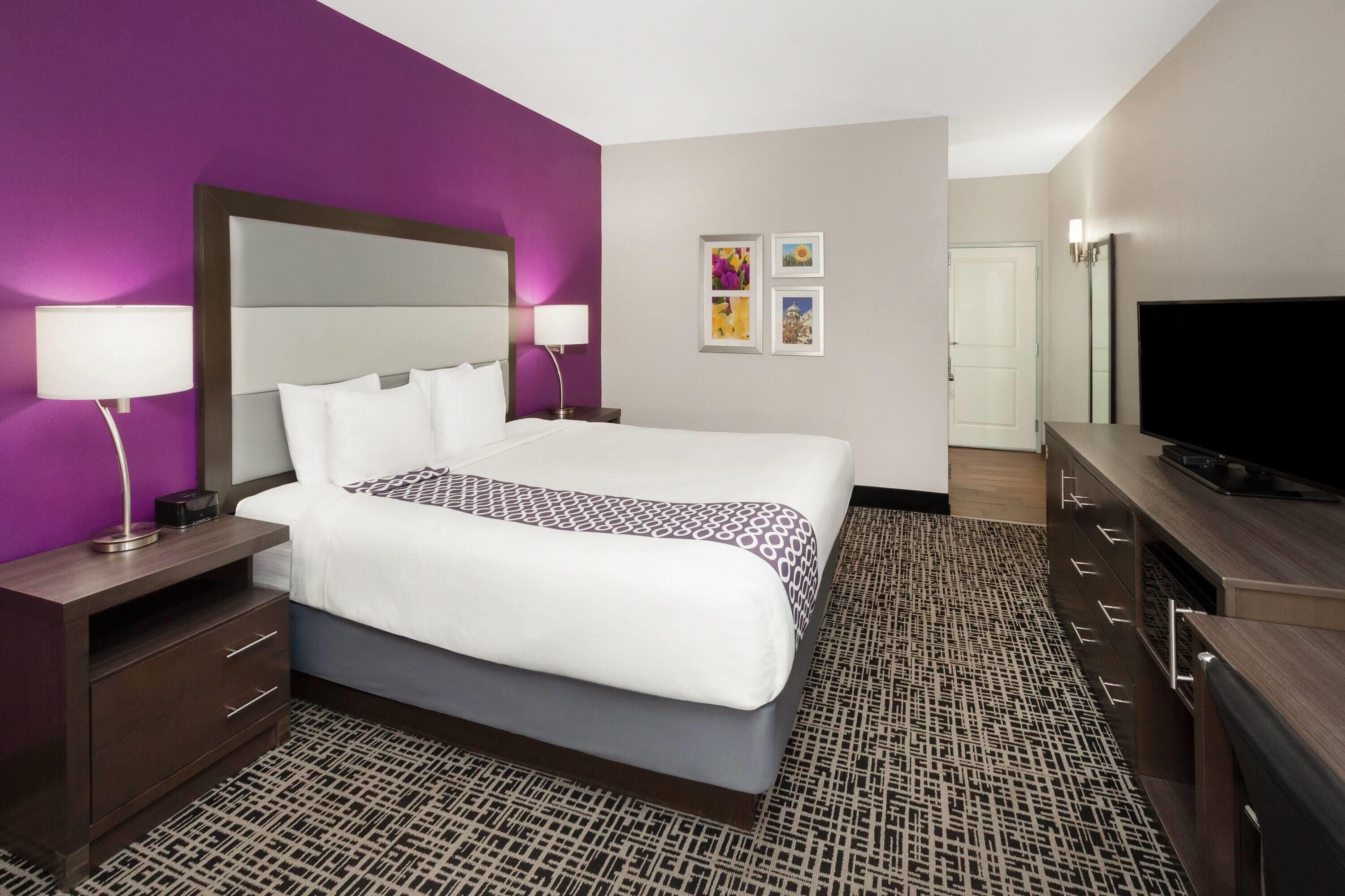 A hotel room with a large bed, a TV, a desk, and a dresser.