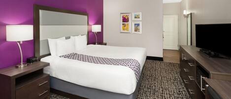 A hotel room with a large bed, a TV, a desk, and a dresser.