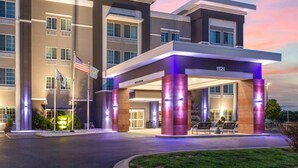 A modern hotel entrance with a covered waiting area, an American flag, and a number '121' sign.