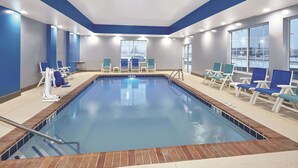 A swimming pool with blue and white lounge chairs arranged around it, a clear view of the pool, and a large window on one side.