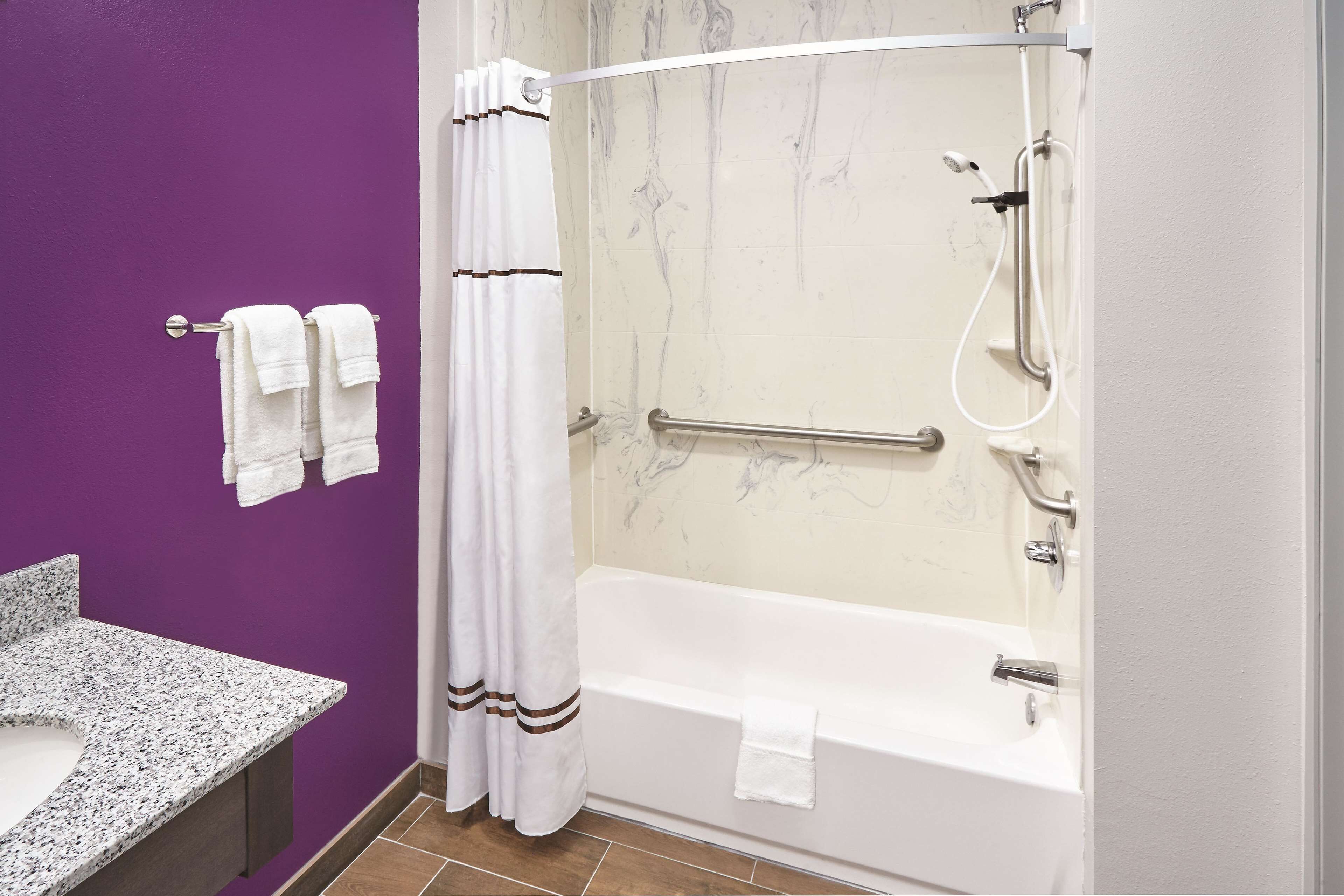A bathroom with a purple wall, a white bathtub, a white sink, and a shower with a glass door.