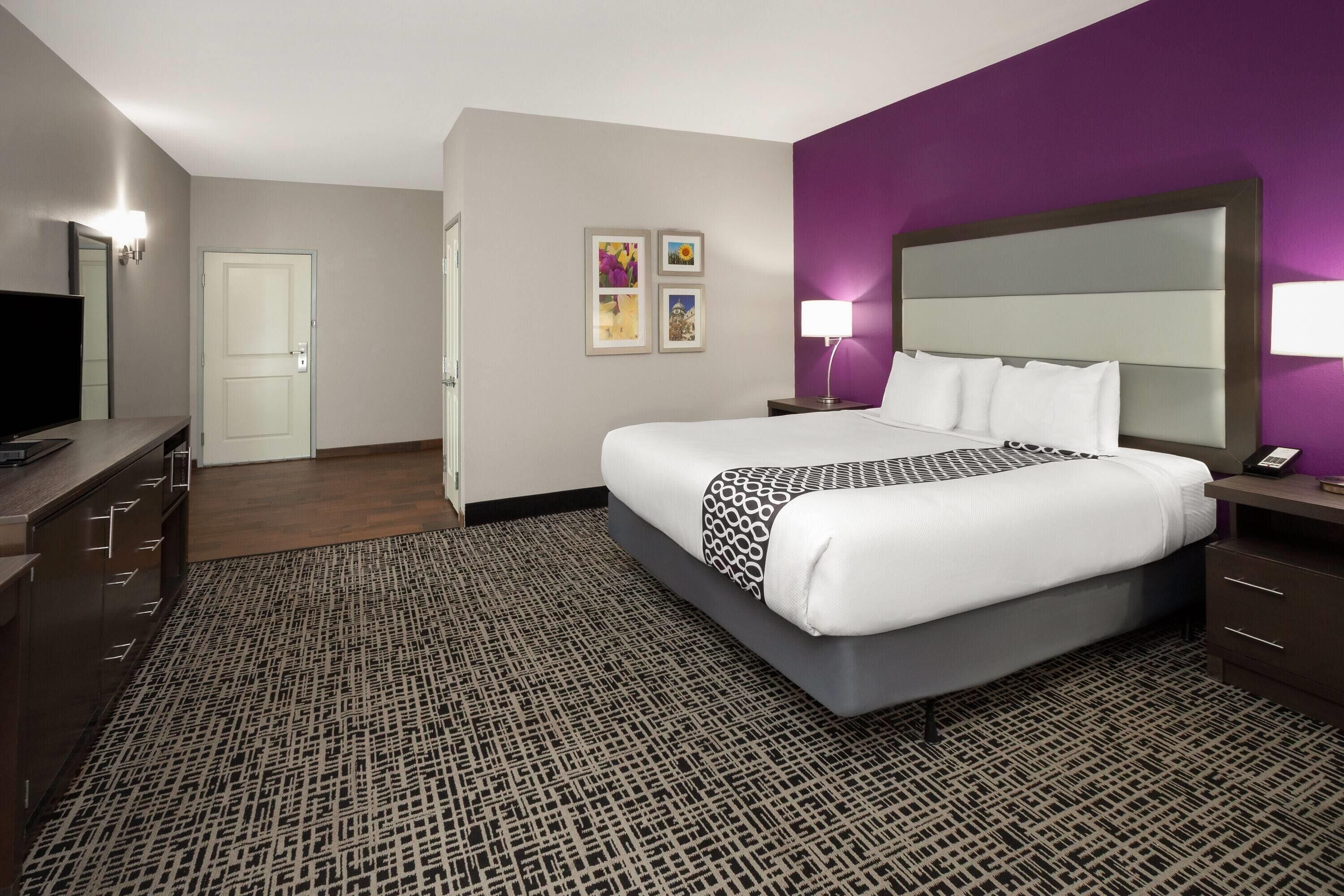 Una habitación de hotel con cama, mesita de noche, lámpara y televisor sobre un aparador.
