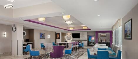 Un hall de hotel con mostrador de recepción, zona de estar y una pantalla de televisión.