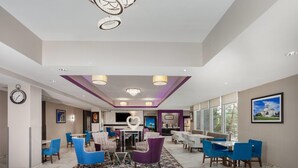A hotel lobby with a dining area, seating arrangements, a clock, and a large window. - La Quinta Inn & Suites by Wyndham Springfield IL (Springfield)