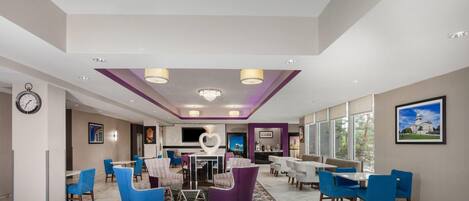 A hotel lobby with a dining area, seating arrangements, a clock, and a large window.