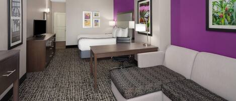 A hotel room with a bed, a desk, a sofa, a TV, and a bathroom.