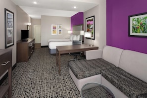Une chambre d’hôtel comprenant un lit, un bureau, un canapé, une télévision et une salle de bain.
