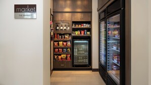 A narrow hallway with a refrigerated display case on the right and a snack display on the left. - Residence Inn by Marriott Houston City Place (Spring)