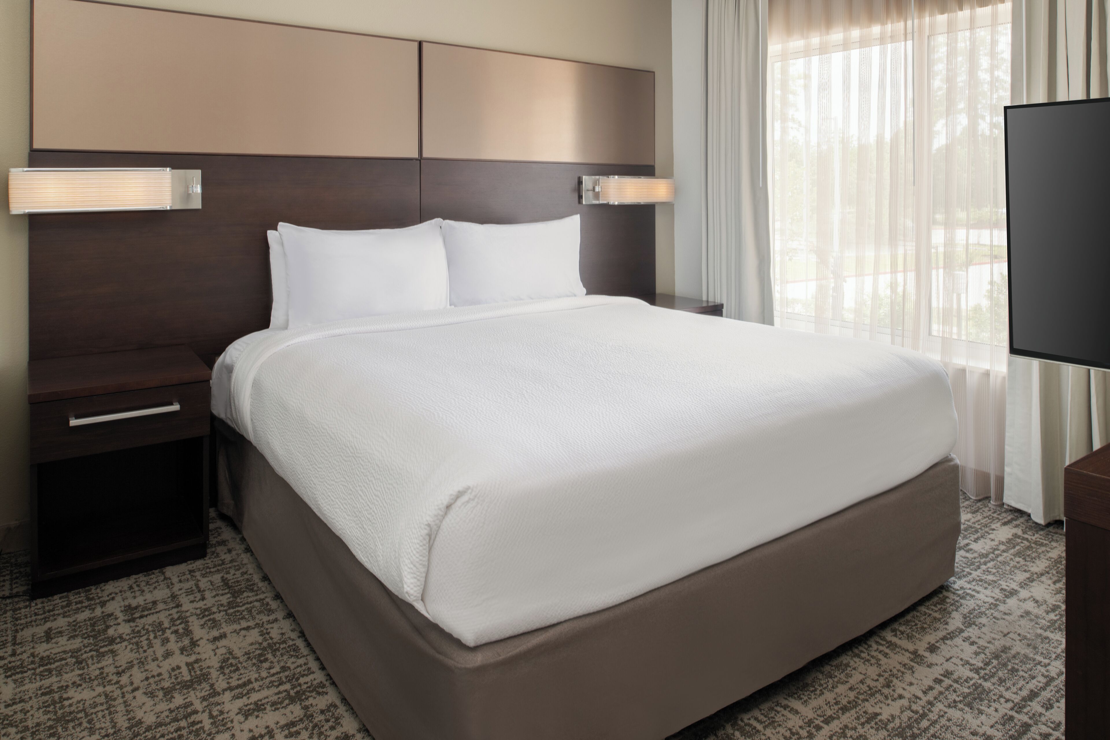 A neatly made bed with a headboard, a bedside table, and a television on a stand.