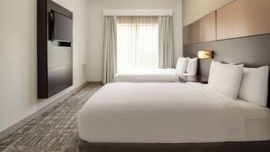 A hotel room with two beds, a flat-screen TV mounted on the wall, a window with curtains, and a headboard with a light fixture. - Residence Inn by Marriott Houston City Place (Spring)