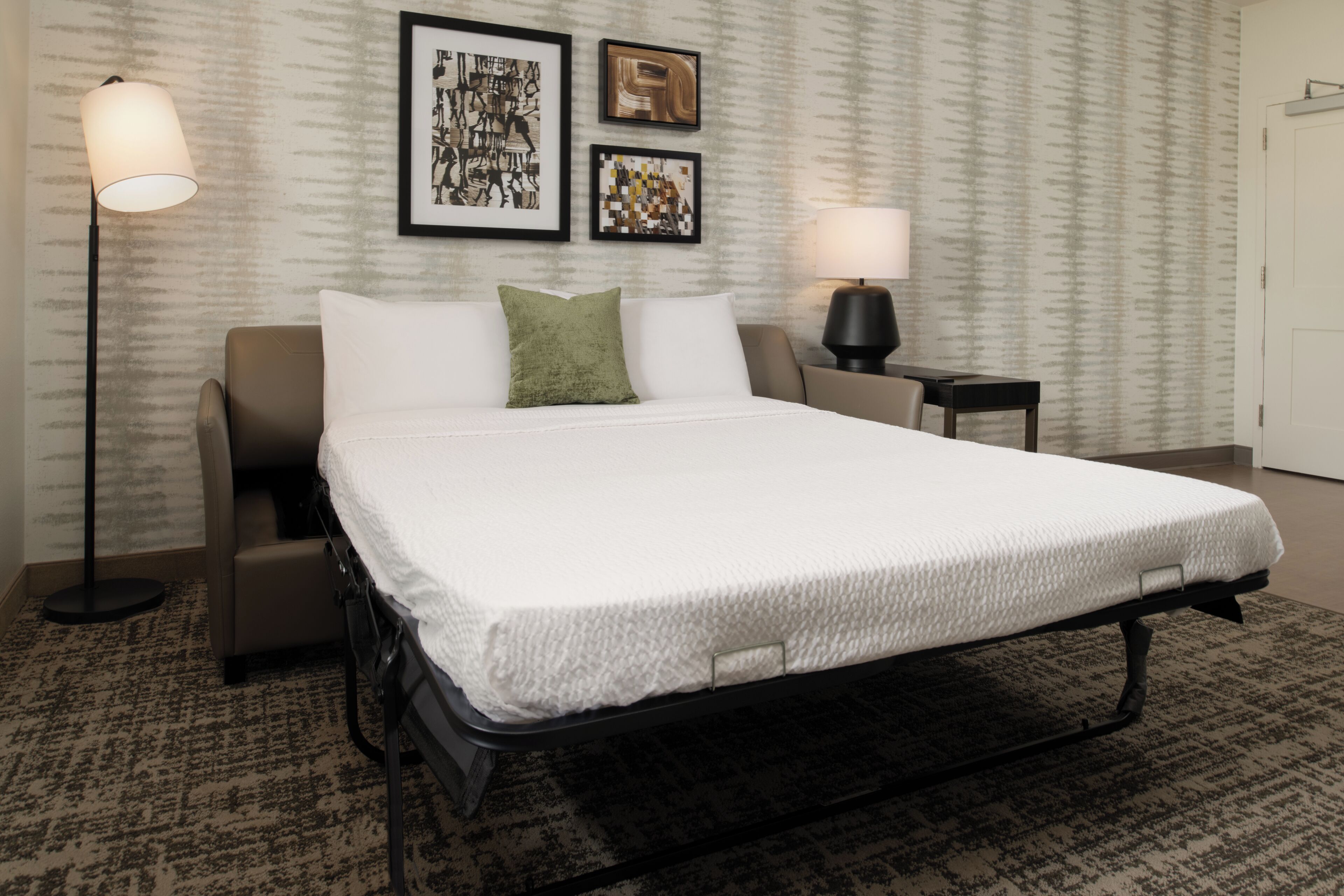 A neatly arranged hotel room with a large bed, a sofa, two side tables, and a lamp.