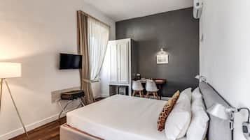 A hotel room with a large bed, a desk, chairs, a TV, and an air conditioning unit.