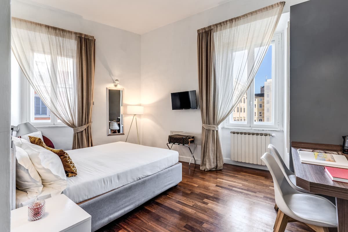 A hotel room with a large bed, a desk with a chair, a television, and a window with curtains.