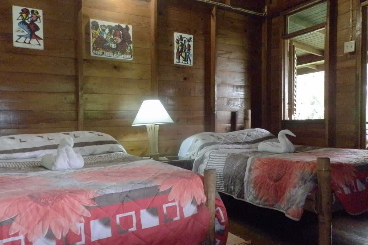 A wooden cabin room with two beds, each with a swan-shaped pillow. There are wall art pieces and a window with a view.