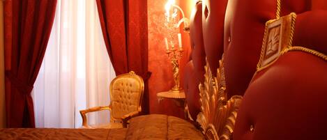 Un dormitorio lujoso con una cama grande, un sillón dorado, un candelabro y cortinas rojas.