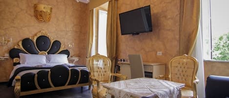 A luxurious bedroom with a large bed, a chandelier, a television, and a dining area with ornate chairs.