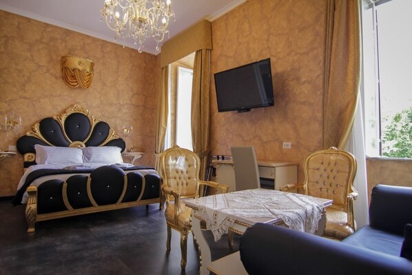A luxurious bedroom with a large bed, a chandelier, a television, and a dining area with ornate chairs.
