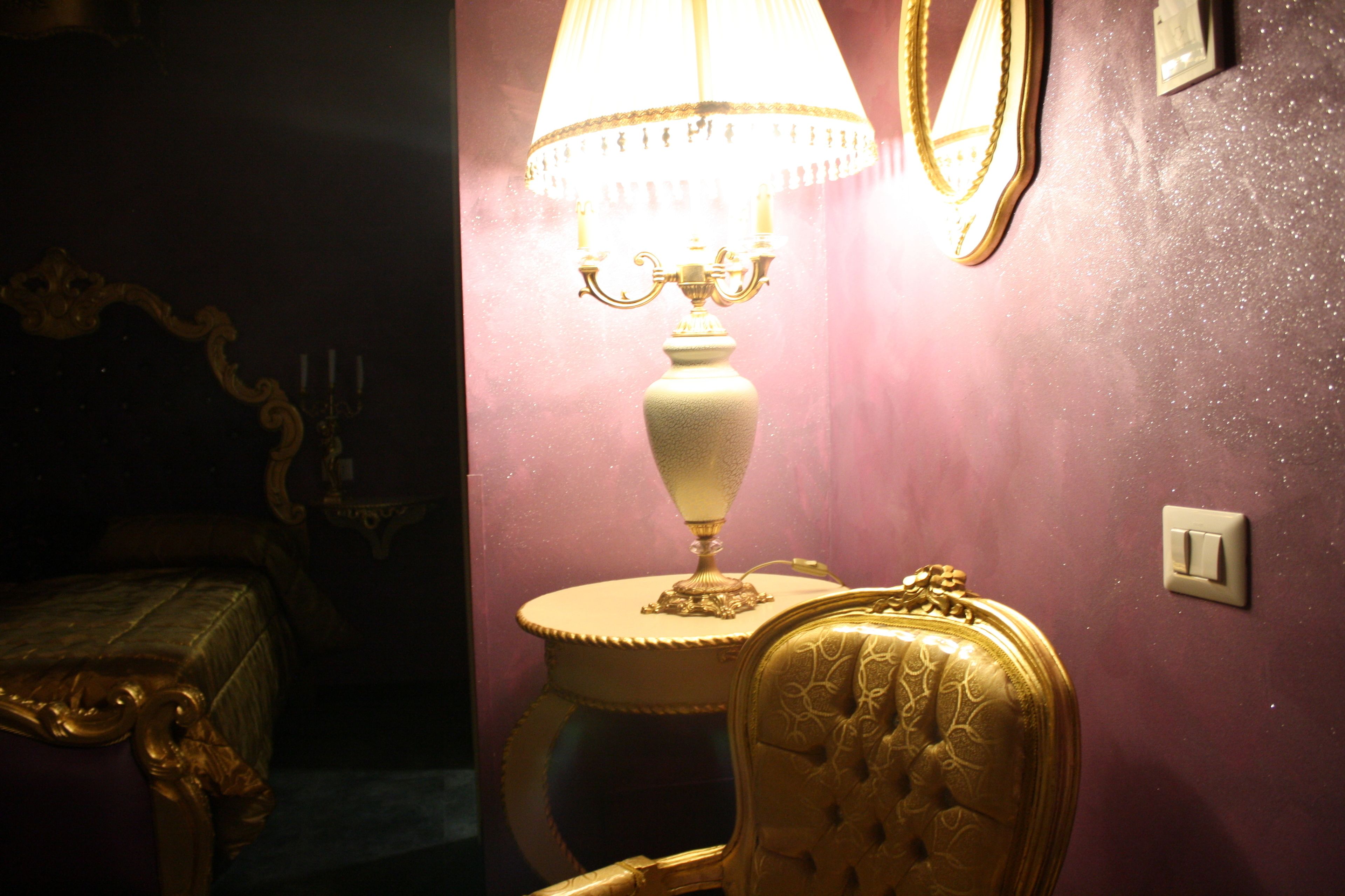 Une pièce comprenant un lit, une chaise, une table avec une lampe et un miroir fixé au mur.
