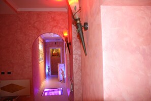 A hallway with pink walls and a marble floor, leading to a room with a bed and a nightstand.