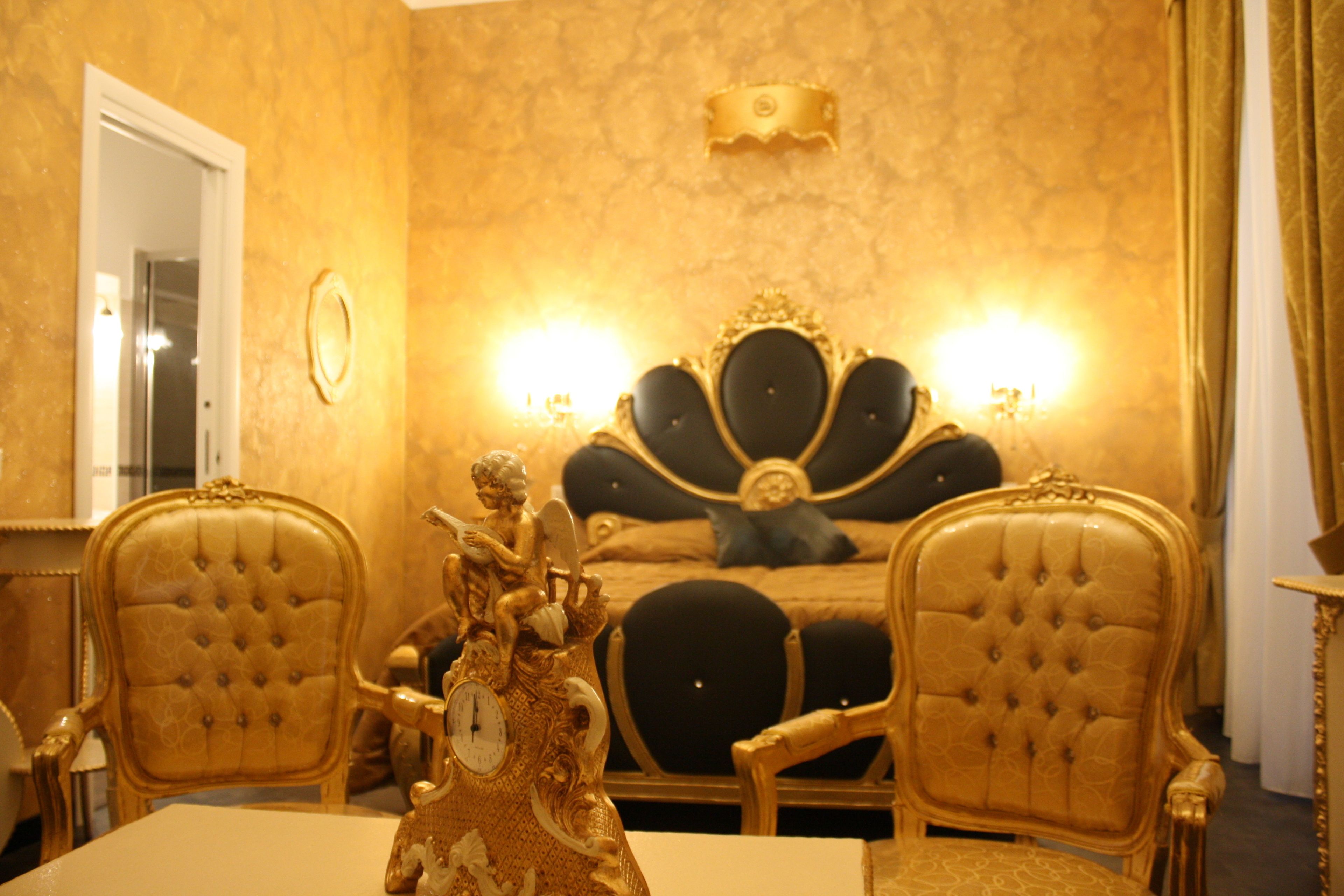 A luxurious bedroom with a large bed, ornate headboard, and two golden chairs.